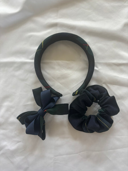 A set of three navy blue fabric hair accessories, including a headband with a small bow and two scrunchies, laid out on a white fabric background.